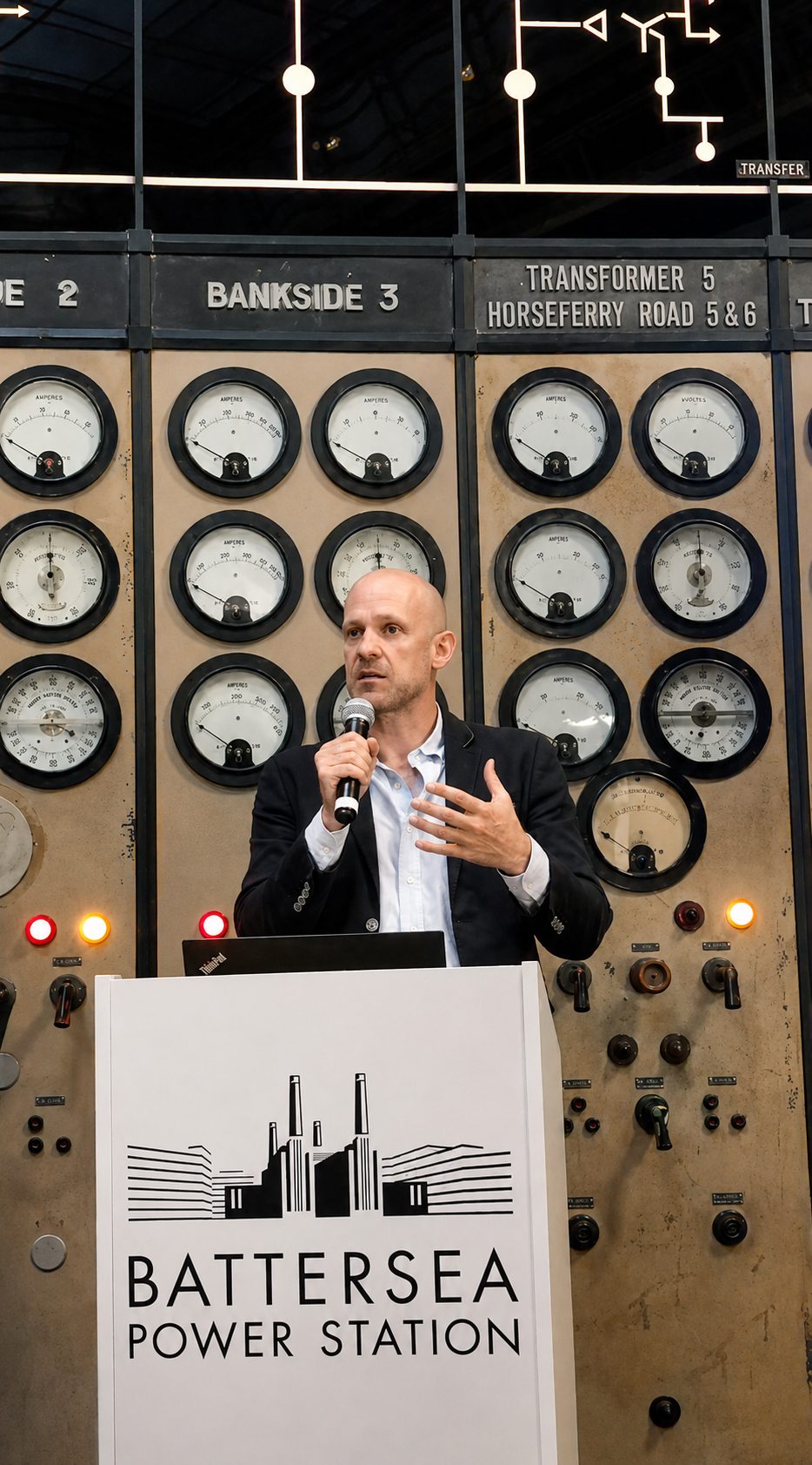 Gordon Adams speaking at a podium in front of the original Battersea Power Station control-room dials